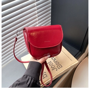 Dettaglio borsa a sella in pelle rossa lucida con logo a rilievo e tracolla sottile