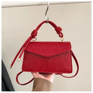 Detail of red textured crossbody bag featuring a unique knotted handle and gold hardware