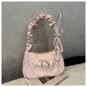 Détail du sac rose montrant la texture marbrée et l'accessoire de nœud doré brillant