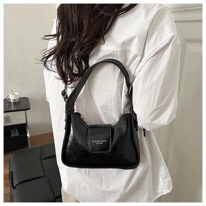 Detail of black patent leather hobo bag with silver lettering on a white shirt model