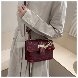 Close-up of deep red crocodile pattern shoulder bag with a gold H-clasp and cherry charm