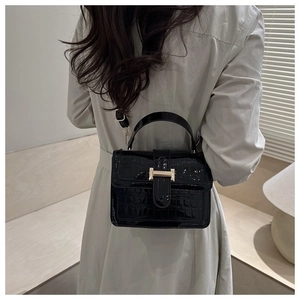Model wearing black crocodile pattern patent leather handbag with gold buckle and beige coat