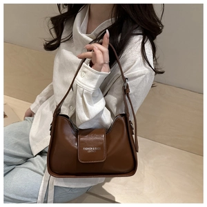 Close-up of brown leather underarm bag with silver fashion text detail on front flap