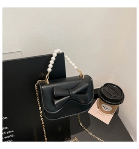 Detail of black mini chain bag with leather bow and white pearl handle ornament