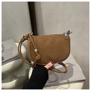 Detailed view of a brown pebbled leather saddle bag featuring a silver zipper and strap