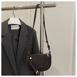 Detail of dark brown saddle bag with knotted strap hanging on a metal rack