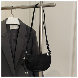 Detail of minimalist black crossbody bag featuring a knotted strap with silver M-bead