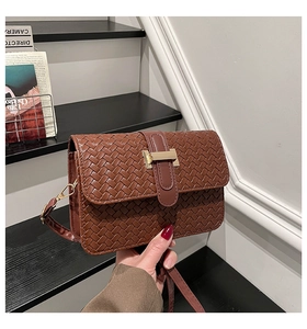 Detailed close-up of brown woven leather texture with golden metal clasp and flap on handbag