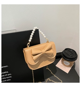 Close-up of beige crossbody bag featuring pearl handle, gold chain and large bow detail