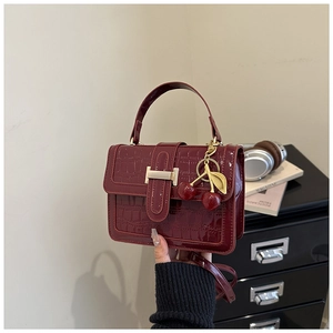 Detail of burgundy crocodile-textured patent leather bag with cherry charm and metal clasp
