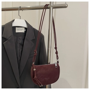 Detail of burgundy matte crossbody bag featuring knot decor and branding on leather