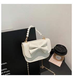 Detail of white bow handbag with pearl handle and golden chain on a black background