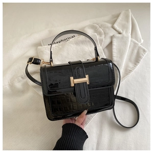 Detail of black faux crocodile leather handbag with glossy finish and gold metal hardware