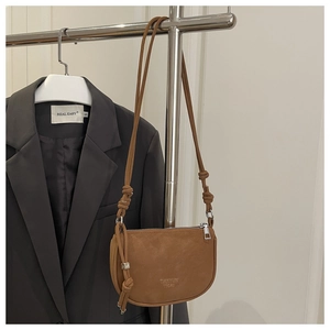 Detail of brown PU crescent crossbody bag featuring knot decor and a metal logo charm