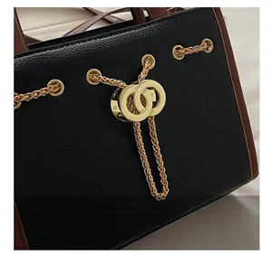 Detail of black pebbled leather handbag with gold hardware and brown trimmed edges