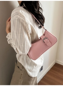 Side view of pink leather underarm bag with silver metal ring buckle on beige shirt
