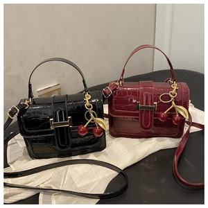 Detail of crocodile pattern faux leather handbags with red cherry charm in black and burgundy