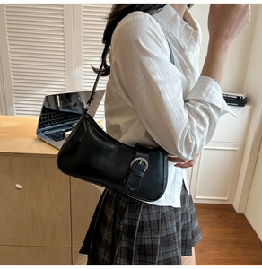 Close-up of black crescent hobo bag with silver buckle worn by a model in a casual setting