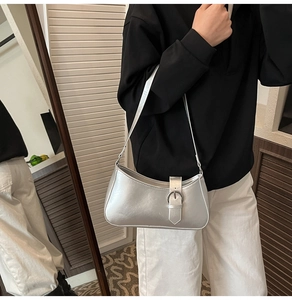 Detail of silver metallic underarm bag with metal buckle worn by a female model