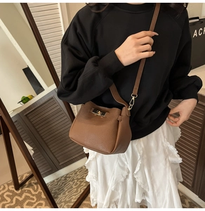 Brown lychee leather bucket bag with gold clasp shown on model with white skirt
