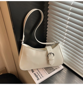Detailed view of white minimalist crescent bag with silver metallic buckle on a windowsill