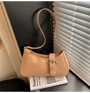Chic beige crescent underarm bag with metal buckle detail on a book by the window
