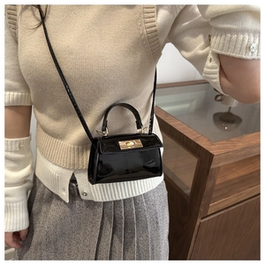 Glossy black patent leather mini bag with gold twist lock shown on beige knitwear