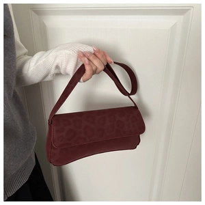 Close-up of a burgundy leopard print suede flap bag held by hand in home setting