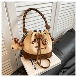 Detail of drawstring bucket bag with plush bear charm and woven handle on white books