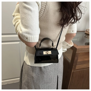 Detail of a black patent leather mini bag featuring gold hardware and a trapezoidal shape