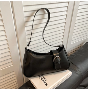 Close-up of black crescent underarm bag with silver metal buckle on a white book