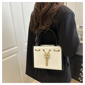 Detailed view of the white leather handbag with gold chain ornament worn with a black suit