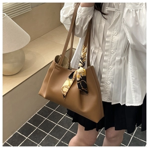 Close-up of brown crescent tote bag with elegant floral silk scarf and leather texture