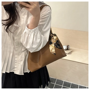 Détail d'un grand sac à bandoulière en cuir marron avec design plissé et foulard en soie