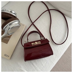 Macro shot of glossy burgundy patent leather mini bag with gold lock and metal rotation clasp
