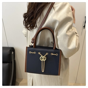 Navy blue tote bag with gold chain and brown handles shown on a model in a stylish interior
