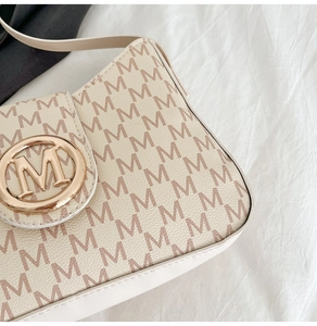 Close-up of golden metal buckle with M logo and letter patterned texture on retro handbag