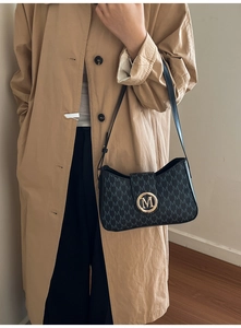Detail of black tote bag with M-pattern texture and golden metal buckle on khaki coat