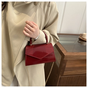 Detail of red patent leather satchel featuring a golden metal chain strap and top handle