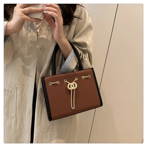 Detail of a brown and black two-tone handbag featuring a gold chain and interlocking rings