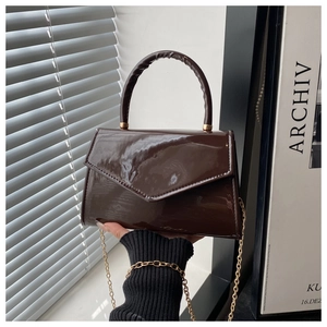 Detail of dark brown patent leather handbag featuring glossy finish and gold chain strap