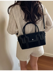 Modern black leather handbag with white contrast stitching worn with a beige suit