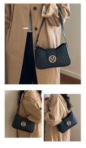Detailed view of black underarm bag featuring embossed M pattern and gold metal buckle