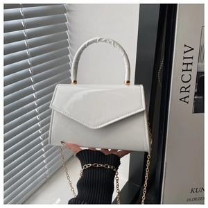 Close-up of glossy white patent leather handbag with gold chain and triangular flap