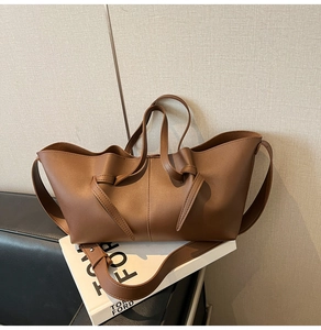 Detail of a brown pleated tote bag with cross-knot decoration on a leather chair