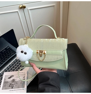 Detail of light green leather bag with gold hardware, plush charm, and detachable strap
