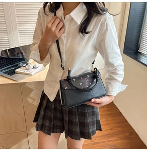 Détail d'un sac bandoulière noir en cuir PU à motifs floraux porté dans un bureau à domicile