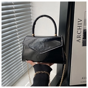 Detailed view of black patent leather envelope handbag with gold chain strap and top handle