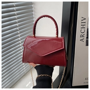 Close-up of wine red patent leather handbag with a triangular flap and gold chain strap