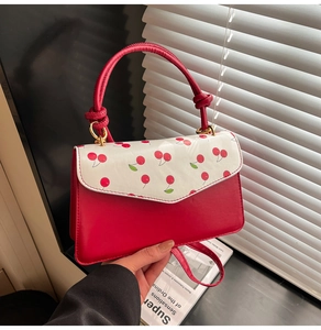 Detailed view of the red crossbody bag featuring cherry print flap and gold hardware
